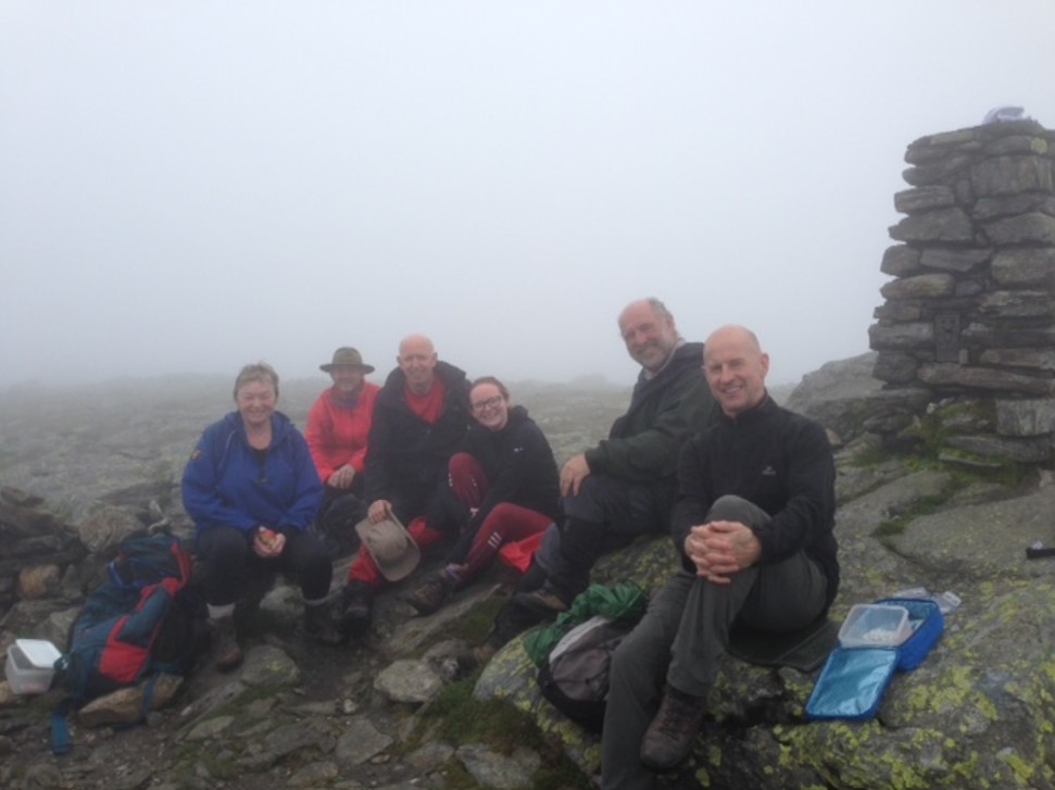 The summit party minus photographer Pete sheltering from the sunshine in the lee of the cairn.